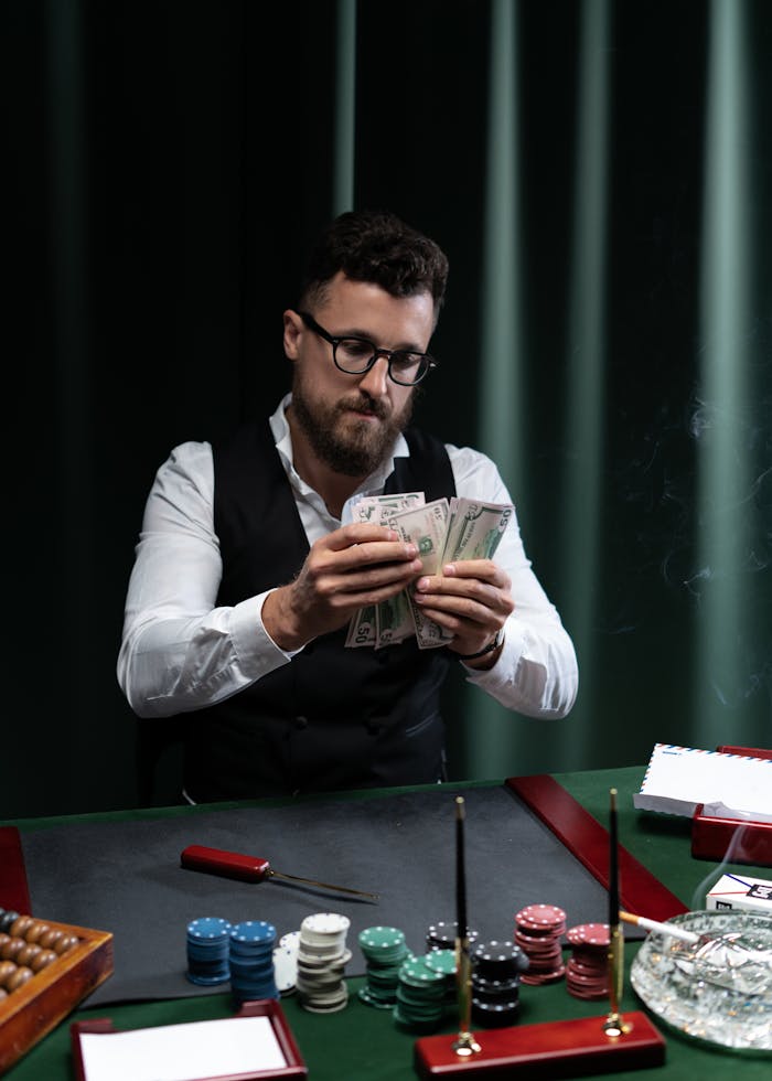 A man at a casino table counting money surrounded by poker chips.
