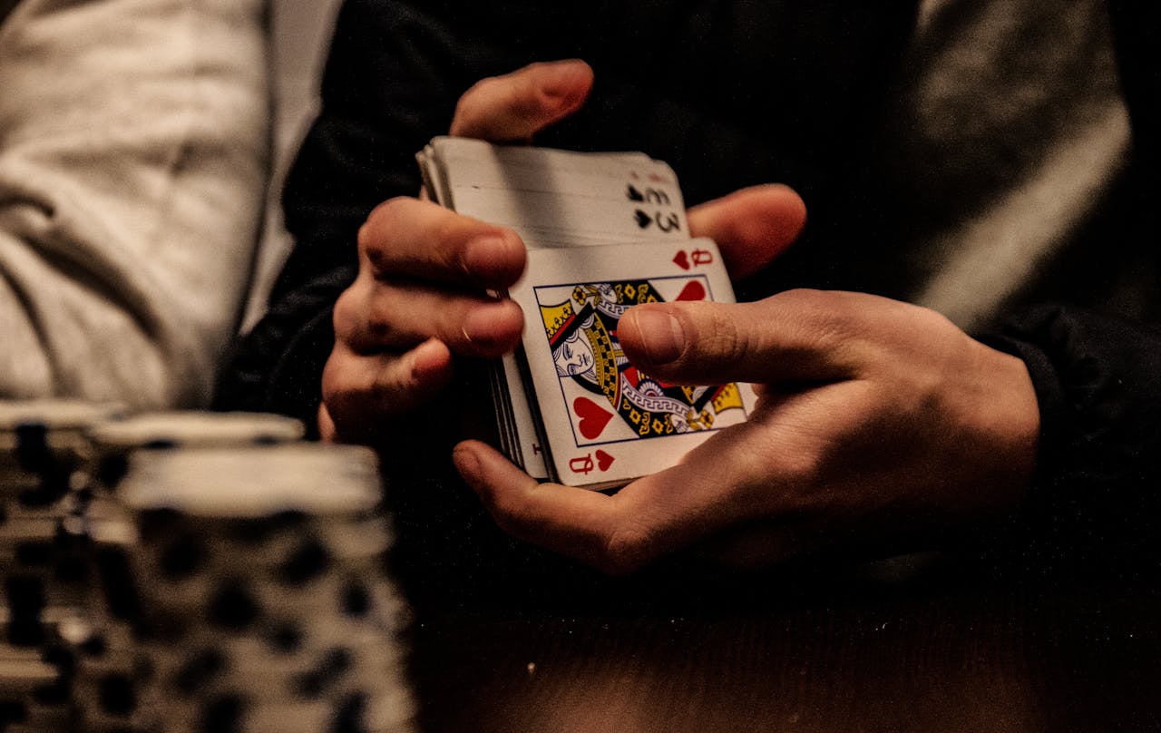Close-up of hands shuffling playing cards during an intense poker game, highlighting the Queen of Hearts.