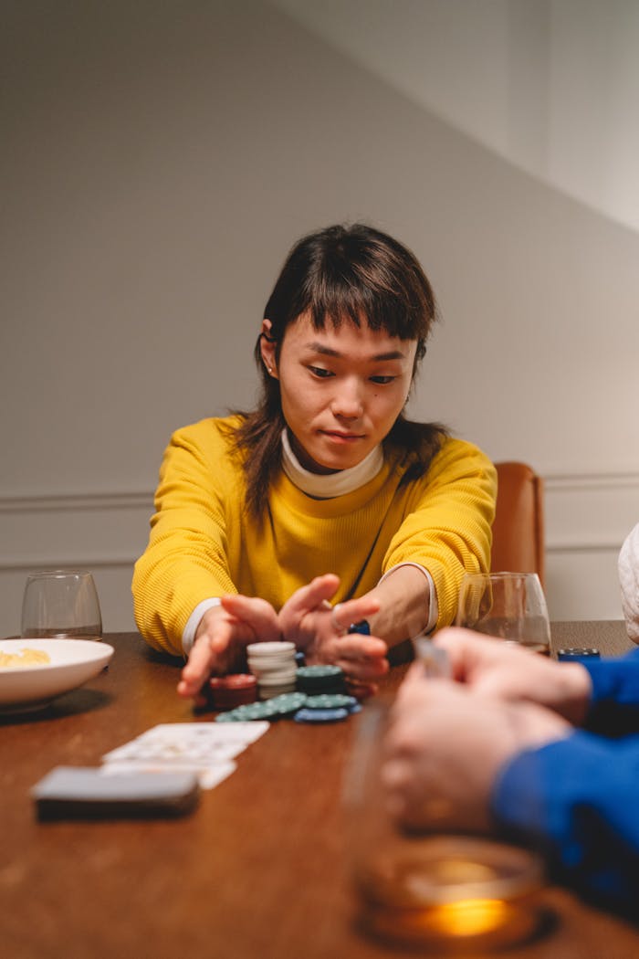 Asian woman enjoying a card game indoors, focusing on poker chips and cards.